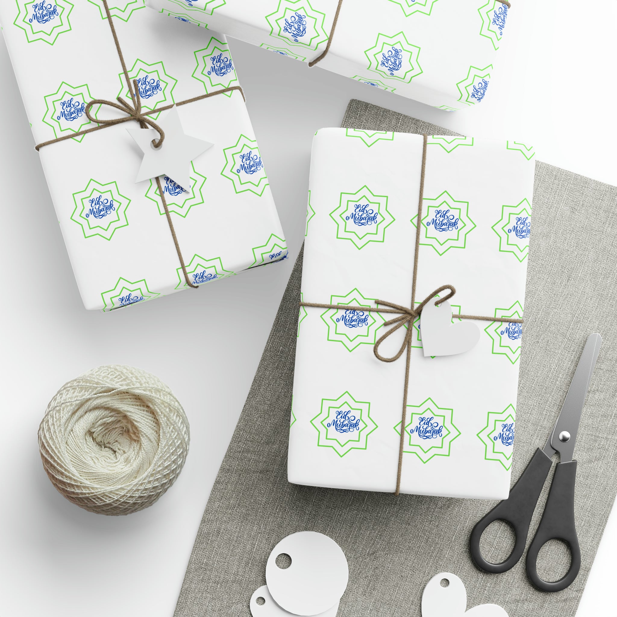 Gift wrapping station with presents wrapped in Eid Celebration Wrapping Paper from Medina Roots, scissors, twine, and blank gift tags on a grey surface for Eid.