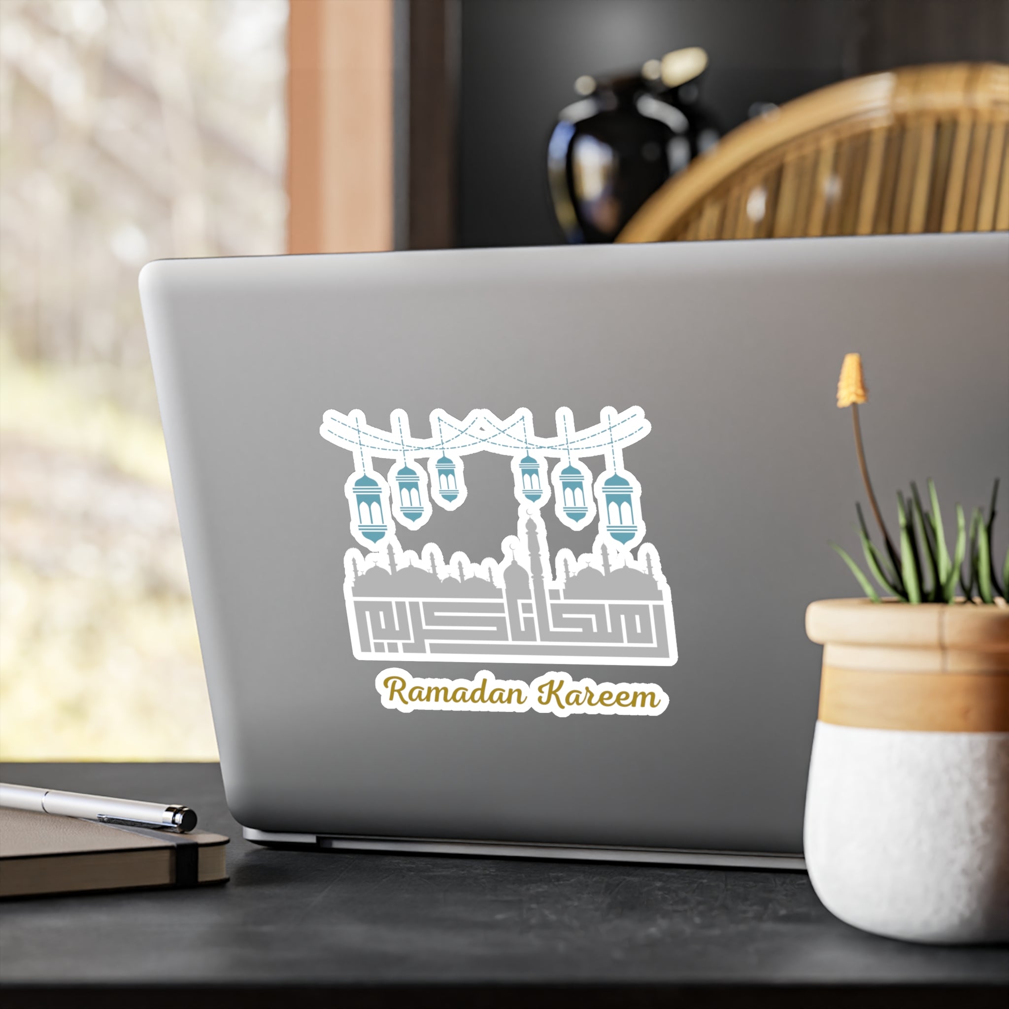 A laptop with a "Ramadan Kareem Kiss-Cut Vinyl Decal" featuring lanterns on its lid, placed on a desk next to a potted plant.