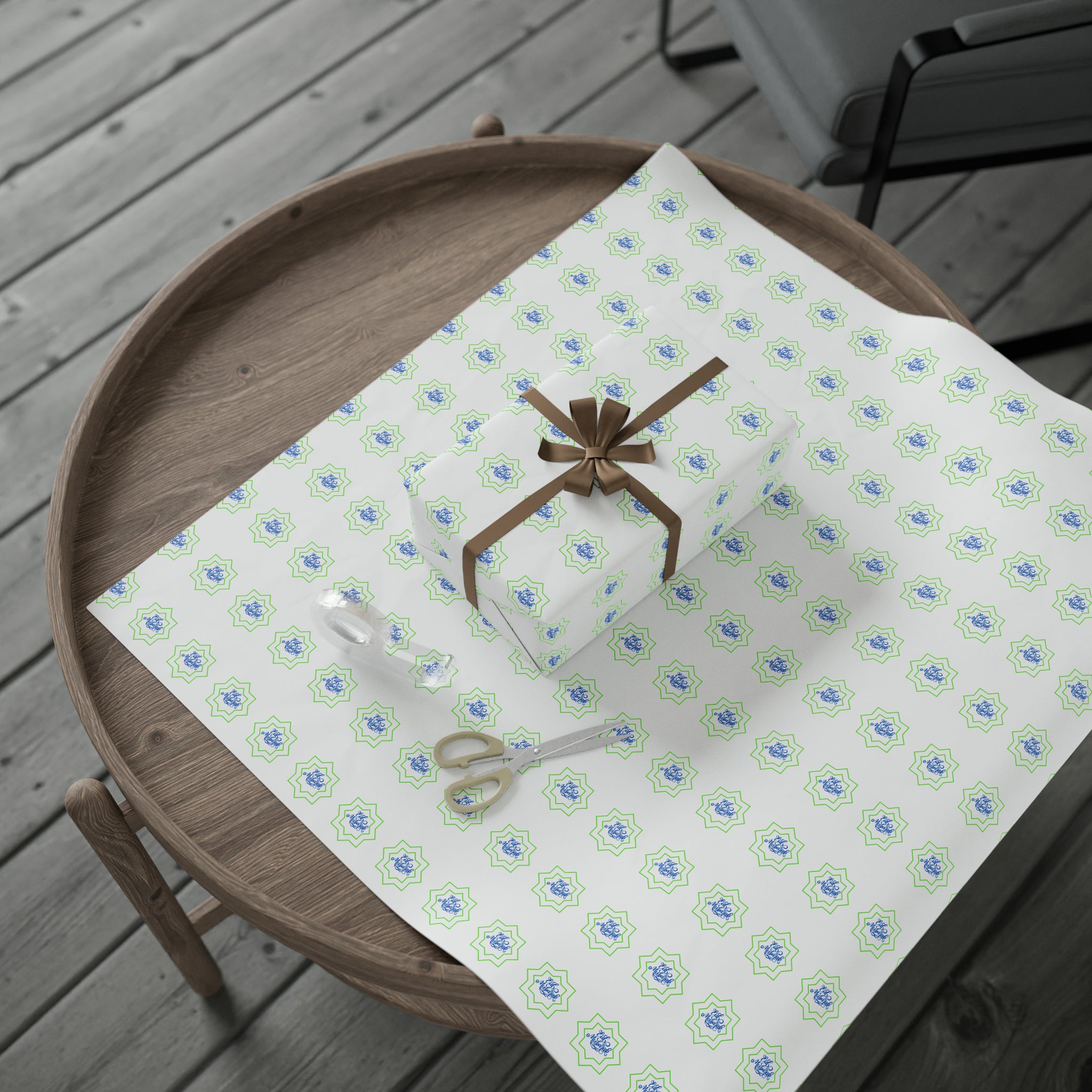 A gift-wrapped box with a brown ribbon lies on a wooden table next to scissors and a roll of "Eid Celebration Wrapping Paper - Ramadan Inspired Design for Meaningful Gifts" from Medina Roots, prepared for Eid celebrations.