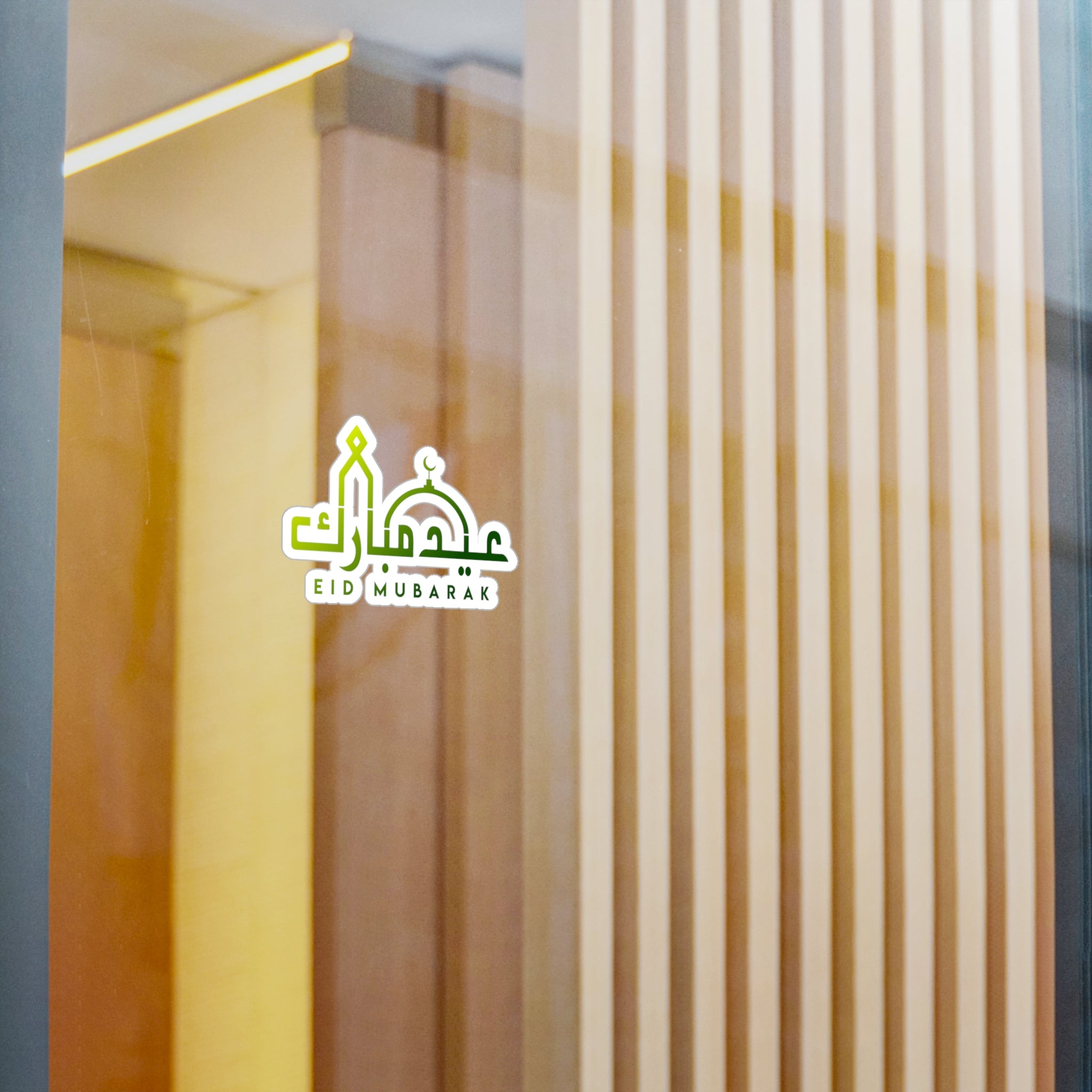 Eid Mubarak" text displayed on a Medina Roots Eid Mubarak Transparent Outdoor Sticker with a blurred background of vertical lines and warm colors.