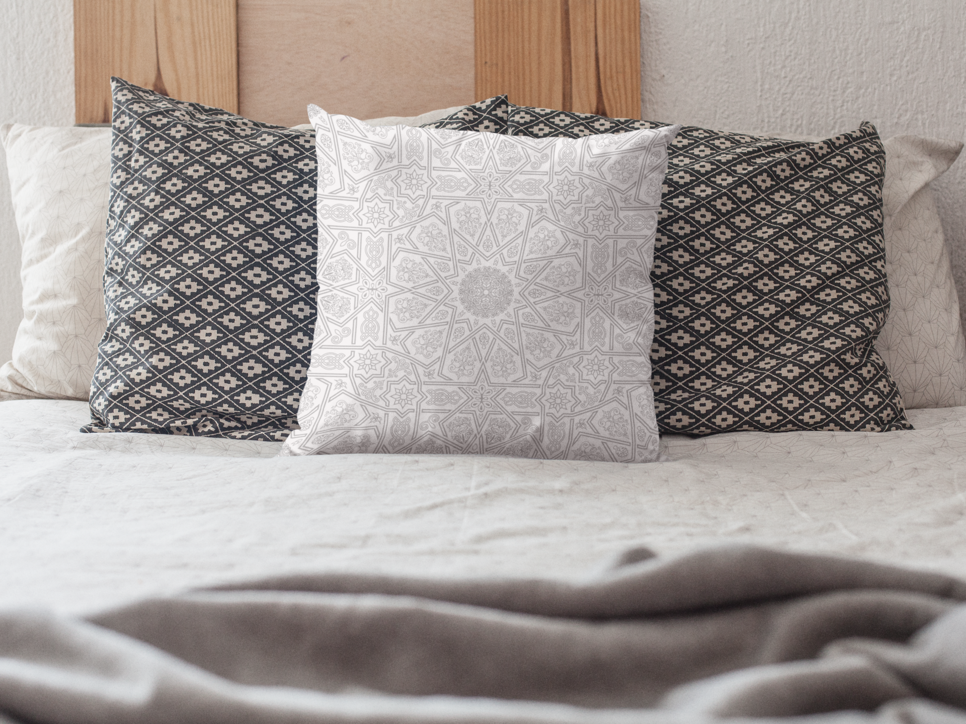 A bed with a grey blanket and a set of patterned pillows, featuring a "Medina Roots" geometric patterned throw pillow cover, arranged against the headboard.