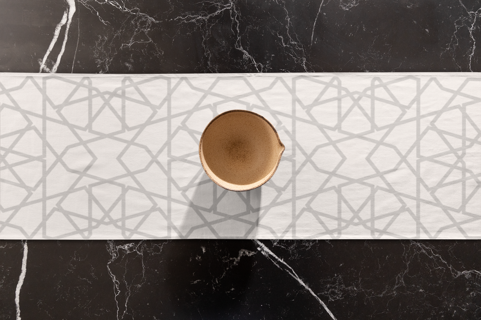 A brown circular object centered on a Vintage-Inspired Geometric Patterned Table Runner by Medina Roots, placed on a dark marble table.