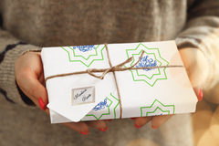 Person offering a gift wrapped with Medina Roots Eid Celebration Wrapping Paper for Eid.